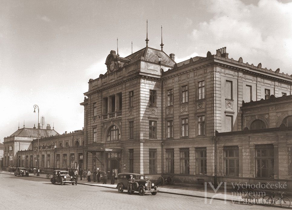 Pardubice, čelní fronta starého nádraží, v popředí osobní automobily, jízdní kola a zastávka autobusů, kolem 1930