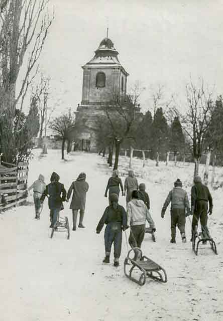 Mikulovice – kostel sv. Václava, děti táhnou sáňky do kopce, 50. léta 20. století